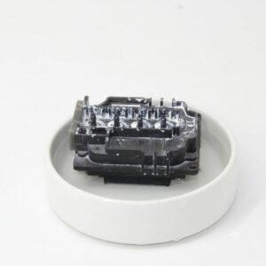 An Epson printhead sitting inside a shallow white dish filled with clear cleaning fluid for maintenance.