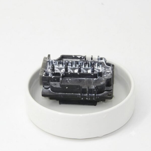 An Epson printhead sitting inside a shallow white dish filled with clear cleaning fluid for maintenance.
