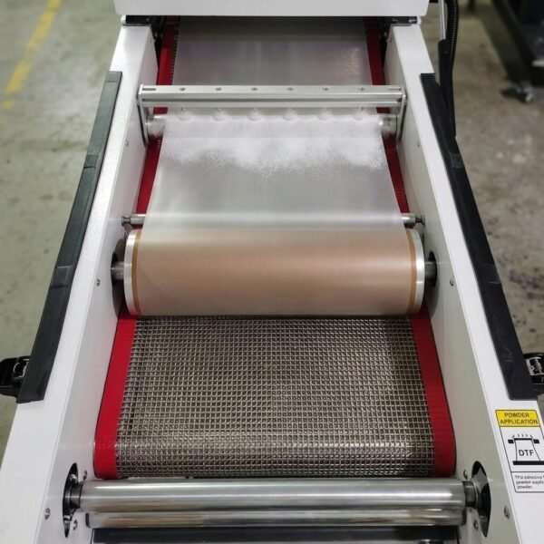 DTF Audley Dual Head I3200 Printer 12 inch with Powder Shaker – High-Precision Mid-Range DTF Printer | ProlificGeeks - Top-down view of a DTF powder shaker showing a stainless steel wire mesh conveyor belt with red borders and feed rollers inside a heating tunnel.