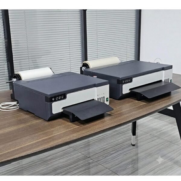 Dual Desktop DTF Printer Setup Two dual-head roll-fed desktop DTF transfer printers sitting side-by-side on a wooden workshop desk with pet film rolls mounted.
